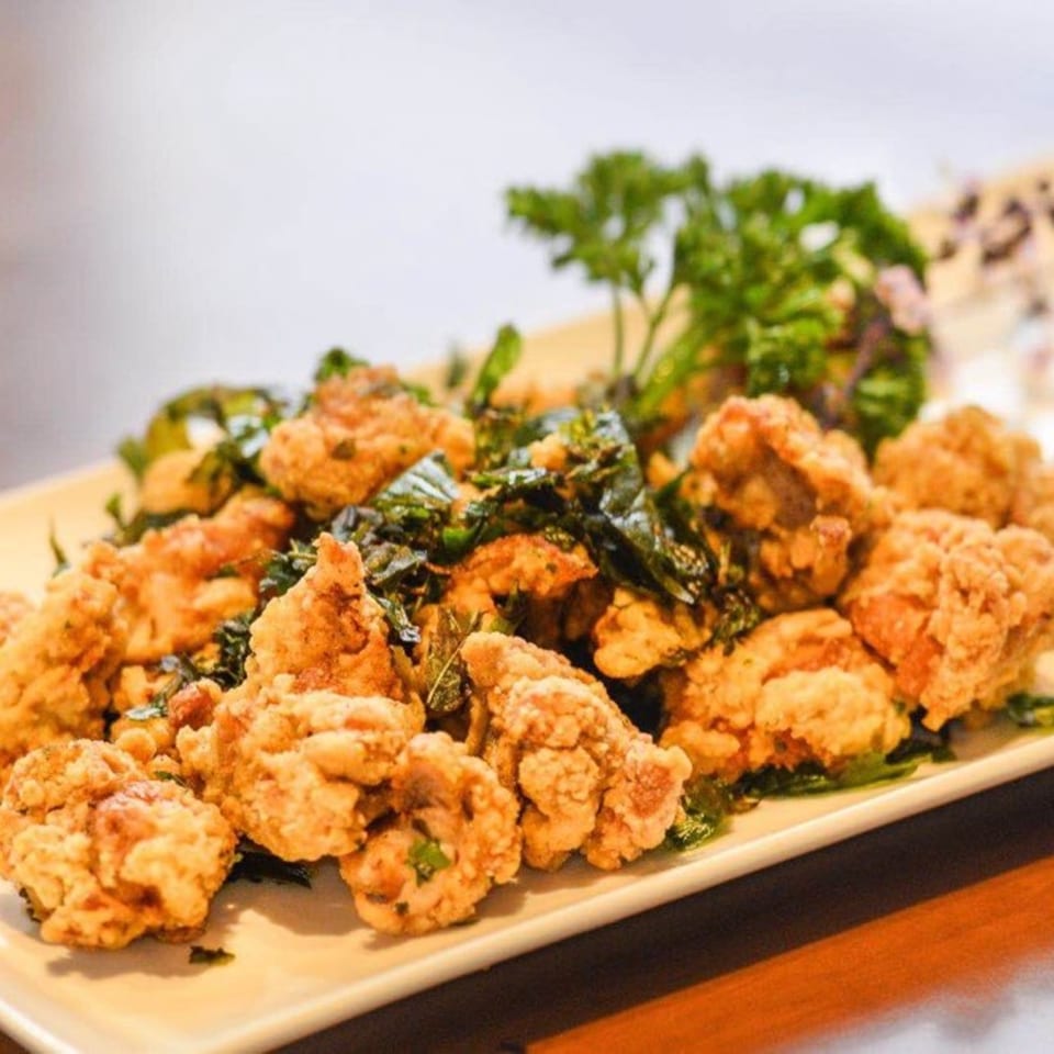 Crispy fried chicken pieces with green herbs on a white rectangular plate at Red Lotus Noodle House.