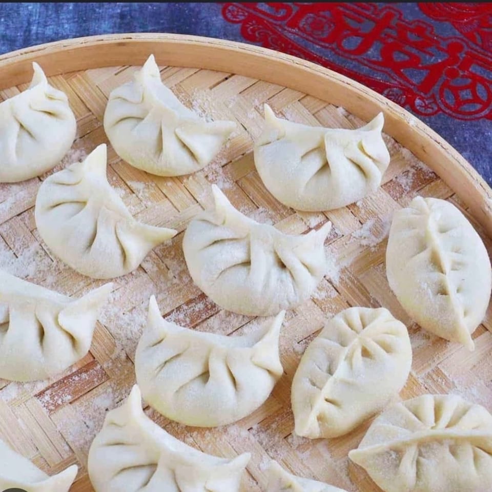 Uncooked Red Lotus Noodle House dumplings, dusted with flour, arranged on a bamboo steamer.