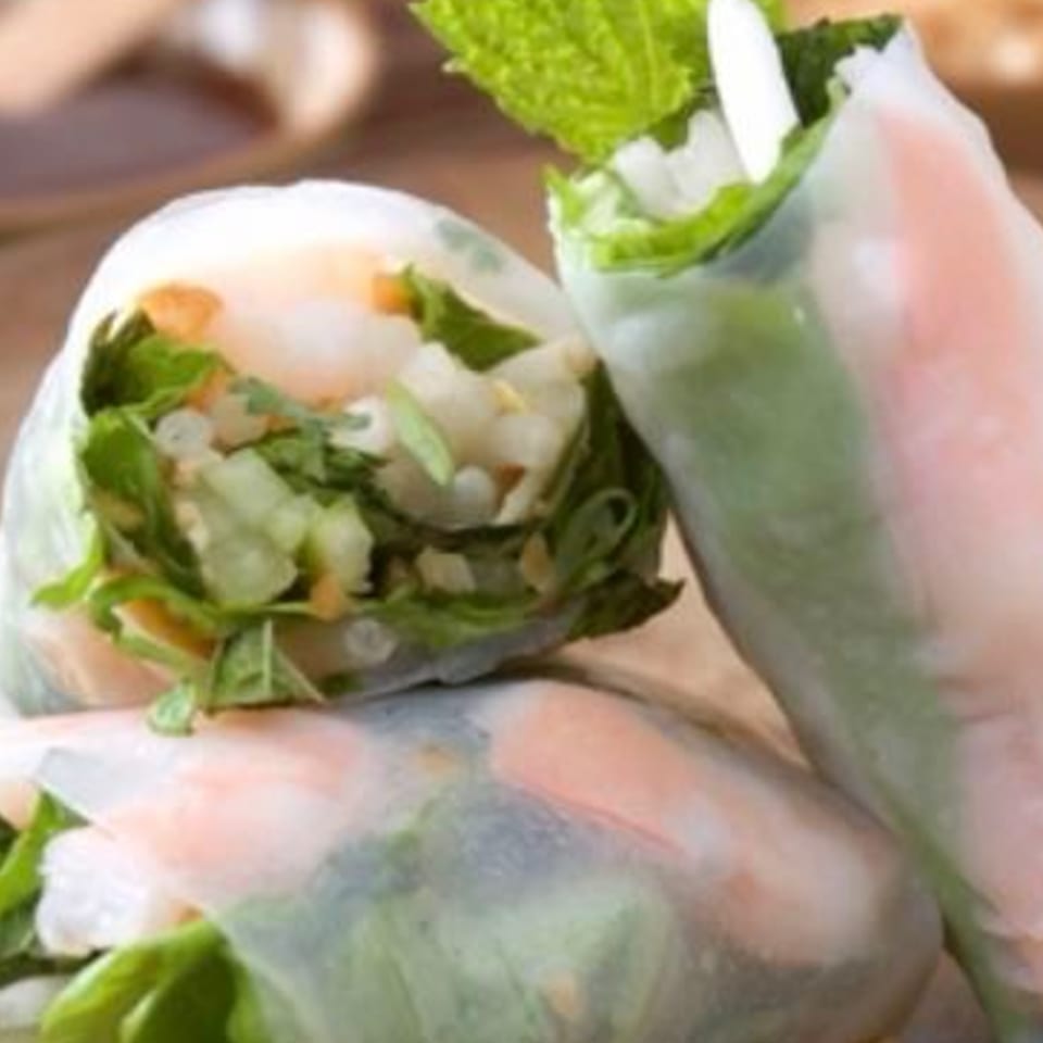Three fresh spring rolls filled with shrimp, greens, and rice vermicelli, garnished with mint.