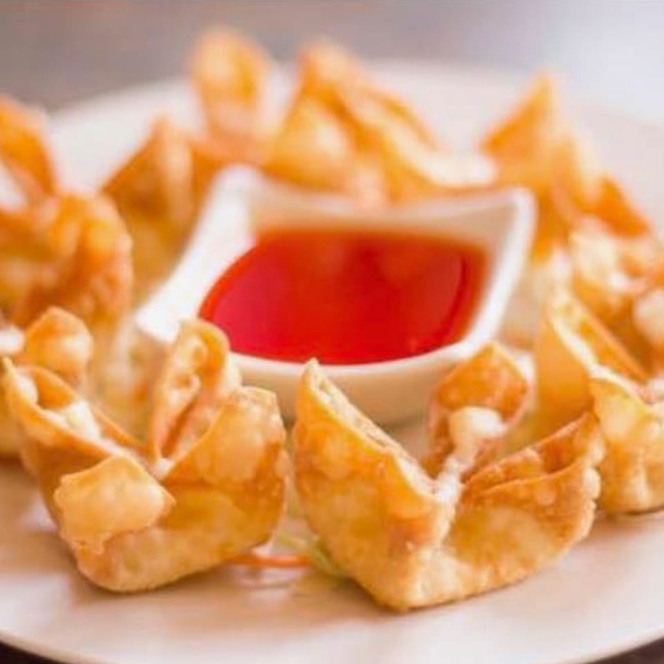 A plate of golden-fried crab rangoon, with a small white bowl of sweet and sour sauce in the center.