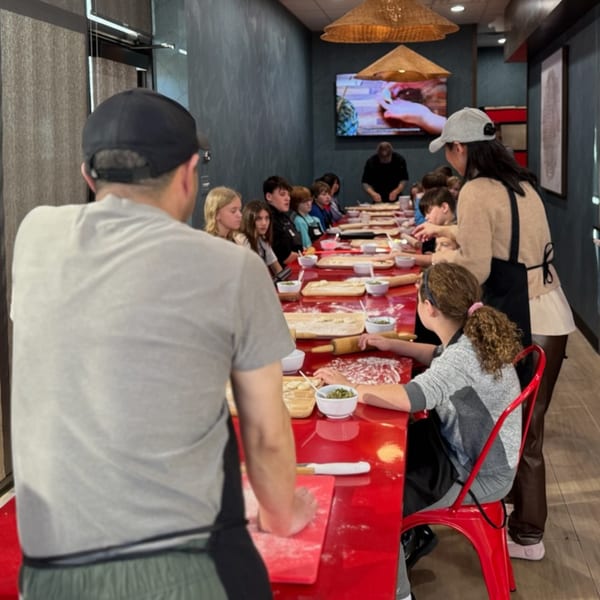Children and adults learning to make dumplings at a long red table in Red Lotus Noodle House.
